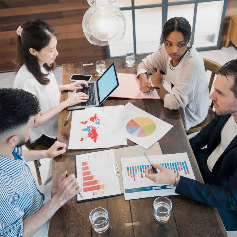 Diverse team in a meeting around a wooden table with charts and a laptop.
