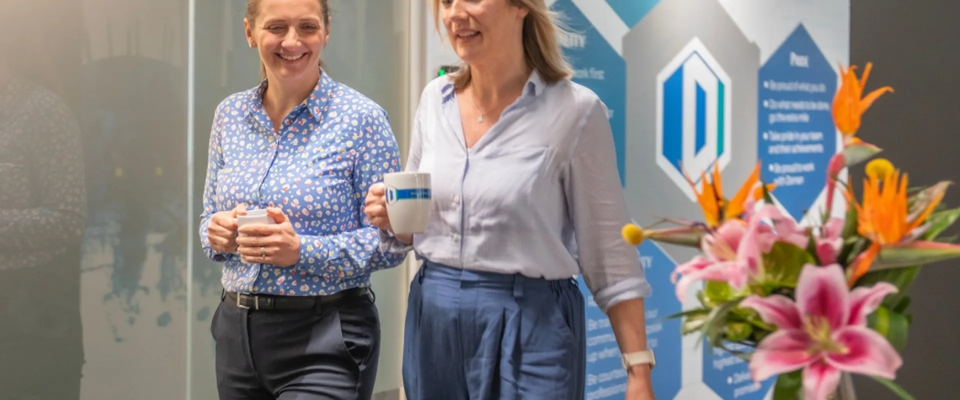 Two employees walking through an office holding drinks, with Dornan values displayed on the wall, representing workplace wellbeing and collaboration.