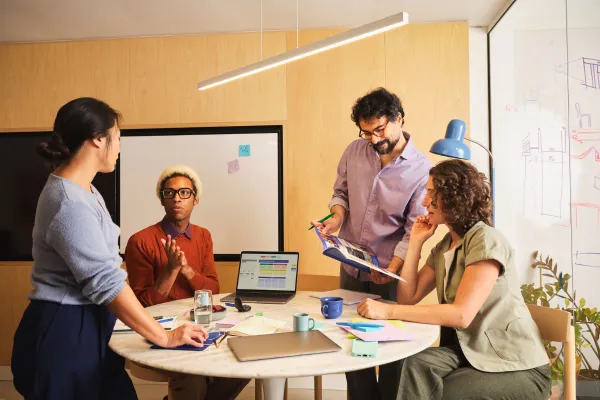 A diverse group of four professionals engaged in a collaborative meeting around a round table in a modern office.