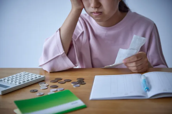 A person in a pink shirt looks concerned while holding a receipt, conveying financial stress.