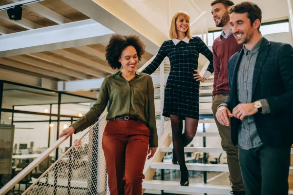 Four people, casually dressed, walk down a modern office staircase, smiling and engaged in conversation, conveying a collaborative and friendly atmosphere.