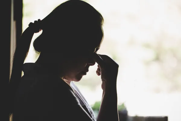 Silhouette of a person. resting their forehead on pinched fingers, expressing stress or contemplation, set against a bright background.