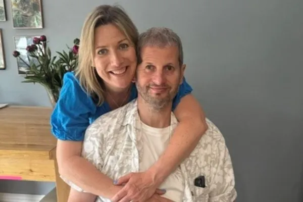 Person sitting in a wheelchair with arm support, embraced from behind by partner at home, reflecting life after stroke and caregiving.
