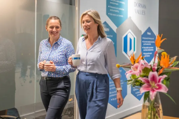 Two employees walking through an office holding drinks, with Dornan values displayed on the wall, representing workplace wellbeing and collaboration.