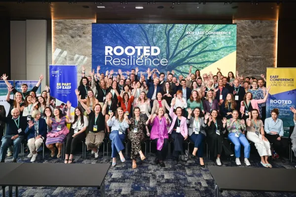 Large group of conference attendees posing in front of ‘Rooted in Resilience’ backdrop at EAEF Conference 2026, highlighting collaboration in workplace wellbeing