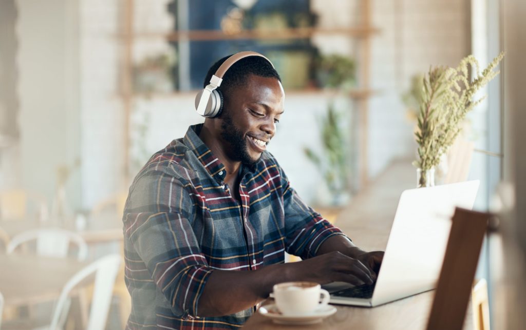 man wears headphones and smiles while working at a laptop