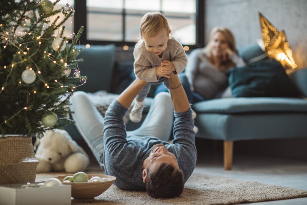 Young daqd plays with daughter on floor next to Christmas tree