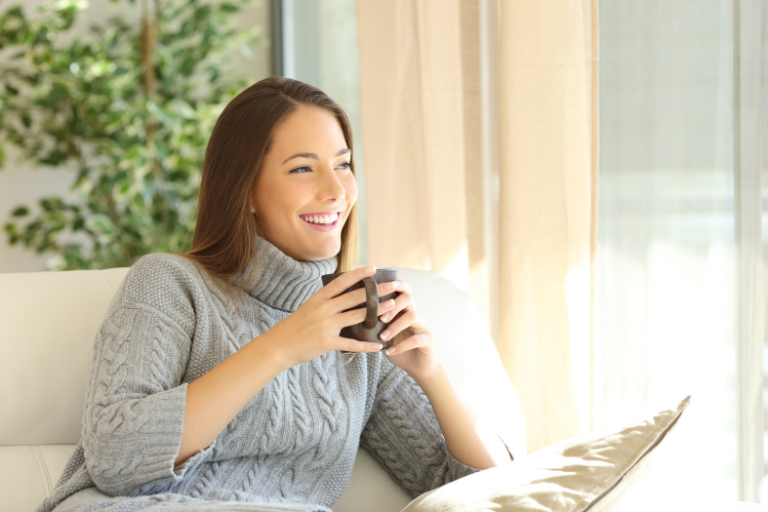 Woman in wooly jumper sitting in a comfy room with a cup of hot drink